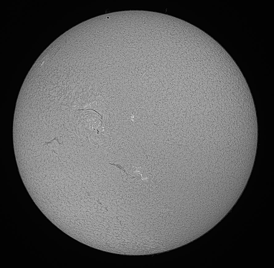 Black&white image of the transit of Mercury on 9 May 2016 as seen in H alpha. Mercury is visible as a small black dot near the upper rim of the Sun.