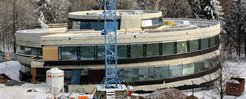 Blick von der Seite auf das im Bau befindliche Haus der Astronomie. Die Fenster sind bereits eingesetzt, aber die Betonstrukturen des Rohbaus sind noch sichtbar.