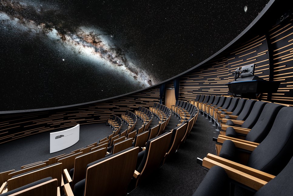 Bildkomposit aus den Sitzreihen des HdA-Auditoriums bei eingeschaltetem Licht und der an die darüberliegene Planetariumskuppel projizierten Milchstraße