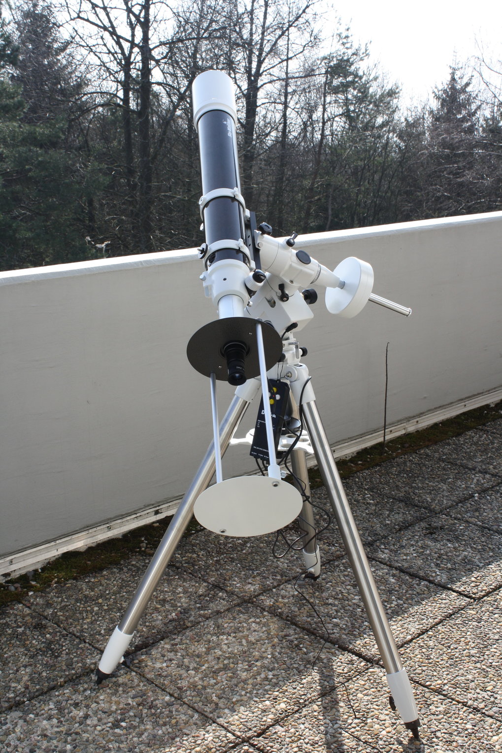 Ein Linsenteleskop mit Sonnenprojektionsschirm auf parallaktischer Montierung steht auf einem Balkon 
