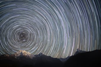 Star trails of many stars, whose circle segments form circles around the northern celestial pole. Below a snowy mountain landscape Star trails of many stars, whose circle segments form circles around the northern celestial pole. Below a snowy mountain landscape