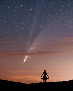 Ein Komet mit Gas- und Staubschweif über dem Horizont mit rötlich angeleuchteten Wolkenstreifen. Davor die Silhouette einer Frau, die ein Kleid trägt und den Rock mit den händen außen festhält
