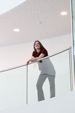 Carolin Liefke mit den Unterarmen auf einer gläsernen Balustrade im Inneren des HdA-Gebäudes abgestützt