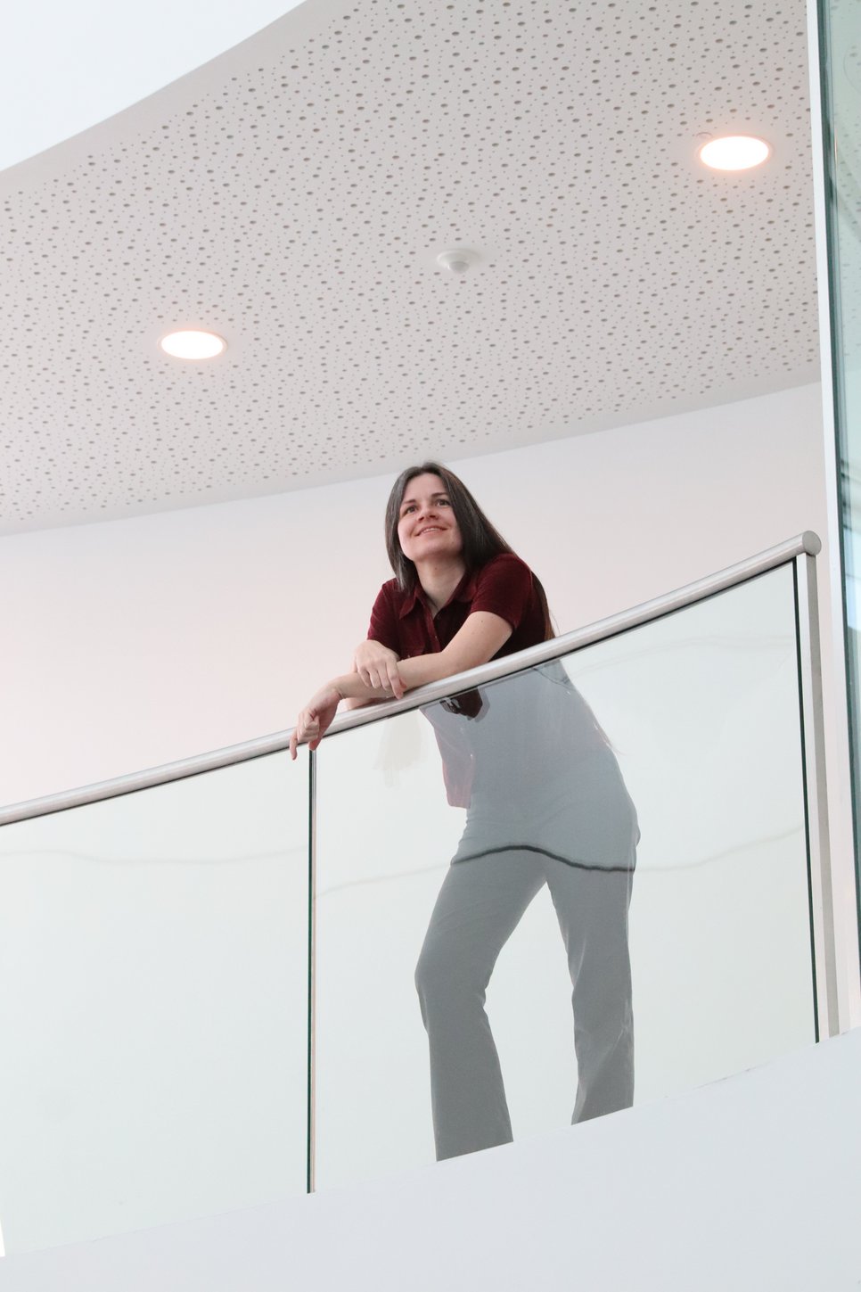 Carolin Liefke leaning on a transparent baluster in the interior HdA building