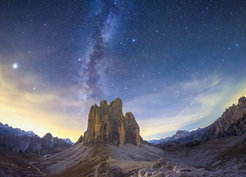 The Milky Way appears as two vertical diffuse bands of light either side of a dark dust lane, over a rocky outcrop