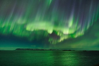 Polarlicht über Island, 3. Platz - Polarlichter (Einzelaufnahmen) Gewellte horizontale grüne Bänder, unterbrochen von dunklen vertikalen Streifen, scheinen fast auf eine Küstenlandschaft niederzuregnen