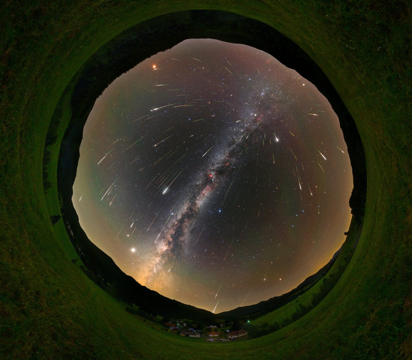 The night sky with the Milky Way in a fisheye view, many shooting stars seem to come from a spot to the upper right of the image center