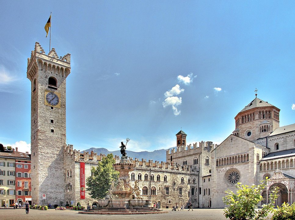 Platz mit alten Gebäuden drumherum. Links ein quadratischer Turm, rechts eine größere Kirche mit einem Kuppel-Überbau